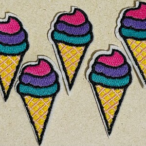 Puede incluir: Cinco parches bordados para planchar en forma de conos de helado en rosa, morado, turquesa y amarillo.