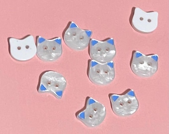 May include: Assortment of white and iridescent cat-shaped buttons with blue ears and eyes.