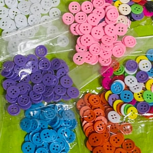 Peut inclure: Assortiment de boutons en plastique colorés de différentes tailles et couleurs, notamment blanc, rose, violet, bleu, orange, jaune et vert. Les boutons sont disposés dans des sacs en plastique.