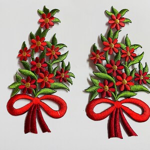 May include: Two embroidered floral patches. Each patch features red flowers with gold centres, green leaves, and a red bow. The patches are likely for decorative purposes, such as embellishing clothing or accessories.