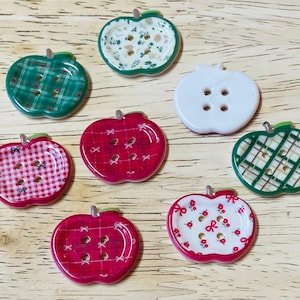 May include: Eight apple-shaped buttons with different patterns. The buttons are red, green, and white with plaid, floral, and polka dot designs.