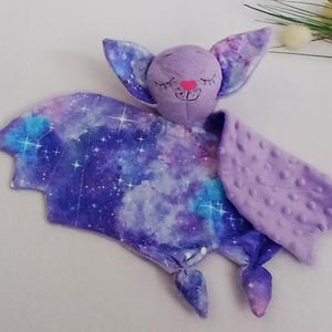 May include: A purple and blue galaxy print bat-shaped baby security blanket with a soft, textured purple back.