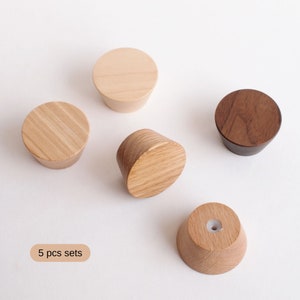 May include: Five wooden wall hooks in different shades of brown. The hooks are round and have a slight cone shape. The text "5 pcs sets" is visible in the bottom left corner of the image.