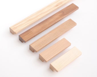Puede incluir: Cinco tiradores de armario de madera en varios tamaños y tonos de marrón. Los tiradores están dispuestos en forma triangular sobre un fondo blanco.