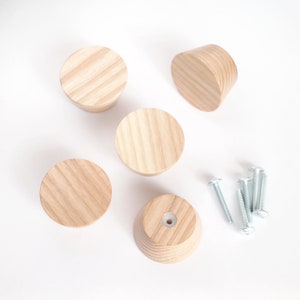 May include: Five wooden knobs with a natural wood finish and a slightly rounded shape. The knobs are arranged in a semi-circle with a set of screws in the center.