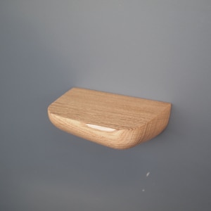 K&ouml;nnte beinhalten: Ein kleines, halbkreisf&ouml;rmiges Wandregal aus hellem Holz mit sichtbarer nat&uuml;rlicher Maserung. Das Regal verf&uuml;gt &uuml;ber eine flache Oberseite und eine abgerundete, geschwungene Vorderkante, die von einer glatten vertikalen Fl&auml;che absteht.