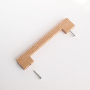 May include: A wooden cabinet pull with a rectangular shape and a simple design. The pull is made of light wood and has two screws for installation.