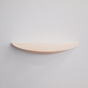 May include: A light-colored, curved wooden shelf mounted on a white wall. The shelf has a smooth, natural finish and a gently rounded shape, perfect for displaying small items. The shelf is approximately 30 inches long.