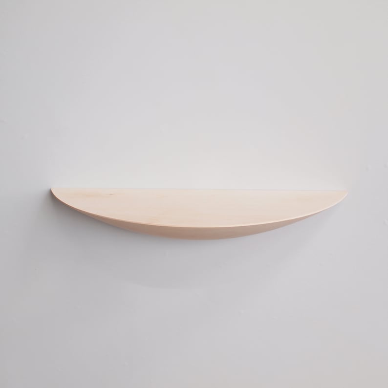 May include: A light-colored, curved wooden shelf mounted on a white wall. The shelf has a smooth, natural finish and a gently rounded shape, perfect for displaying small items. The shelf is approximately 30 inches long.