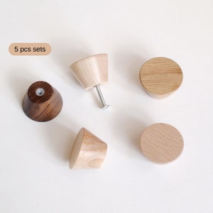 May include: Set of five wooden knobs in two different styles. Three knobs are round and two are cone-shaped. The round knobs are light brown and the cone-shaped knobs are dark brown and light brown. The knobs are shown on a white background. 5 pcs sets