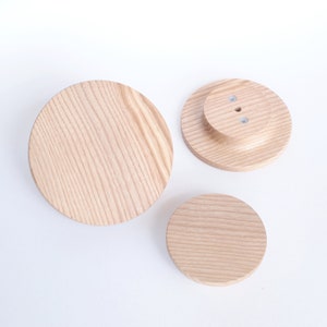 以下が含まれることがあります： 木目模様の丸いコースターが3つあります。一番大きいコースターはシンプルですが、他の2つは中央が盛り上がっていて、中央に小さな穴が開いています。
