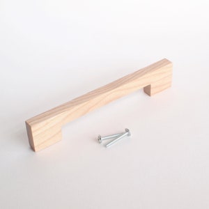 May include: A light wood cabinet pull with a rectangular shape and a slightly beveled edge. The pull comes with two silver screws.