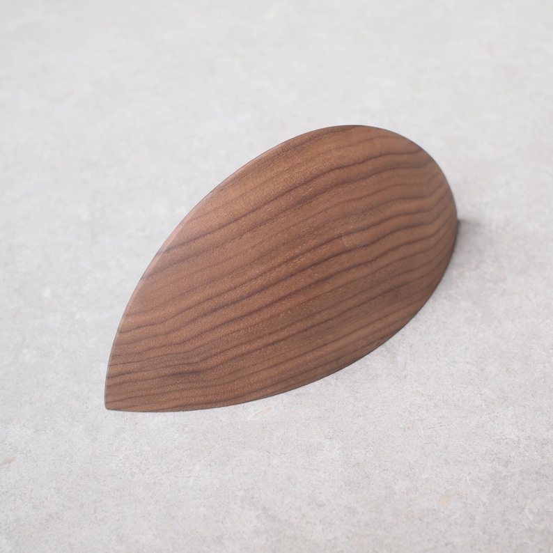 May include: A teardrop-shaped wooden object with a rich brown color and visible wood grain. The smooth, curved surface suggests a handcrafted item, possibly a decorative piece or a kitchen utensil.