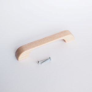 May include: A light wood cabinet pull with a rounded rectangular shape and a slightly curved top. Two silver screws are included.