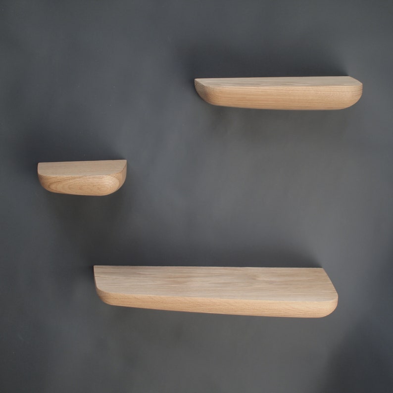 K&ouml;nnte beinhalten: Drei Wandregale aus hellem Holz mit einer glatten, abgerundeten Vorderkante und einer nat&uuml;rlichen Holzmaserung. Die Regale sind versetzt angeordnet, mit einem kleinen Regal auf der linken Seite und zwei gr&ouml;&szlig;eren Regalen auf der rechten Seite.