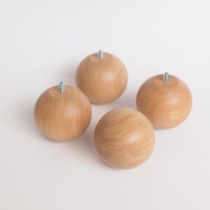 May include: Four wooden furniture legs, each a light brown sphere with a metal screw protruding from the top. The legs are made of wood and are designed for furniture. The legs are evenly spaced against a white background.