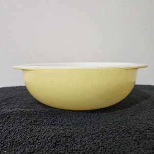 May include: A yellow speckled ceramic bowl with a white interior. The bowl has a rounded shape and a slightly flared rim.