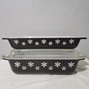 May include: A set of two black casserole dishes with white snowflake designs. The dishes are stacked on top of each other.