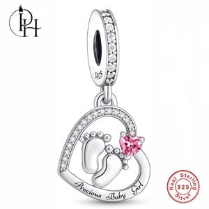 May include: A sterling silver charm featuring a heart-shaped frame encrusted with clear stones. Inside the heart are two polished baby footprints and a small pink heart-shaped stone. The text "Precious Baby Girl" is engraved at the bottom.
