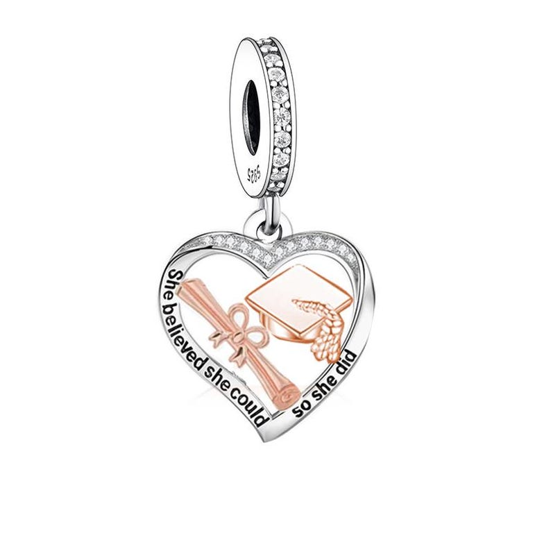 May include: Silver charm with a heart-shaped pendant. The pendant features a graduation cap and diploma in rose gold, with the words "She believed she could so she did" in a cursive font. The charm has a loop with clear crystals.