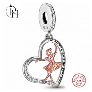 May include: A silver heart-shaped charm featuring a rose gold-toned ballerina figure in the centre. The heart frame is accented with small clear stones and engraved with the text Be strong and Be yourself. The bail is stamped with S925.