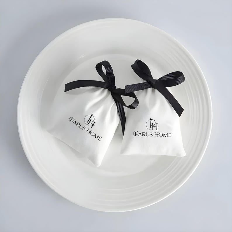 May include: Two small white fabric pouches with black ribbon ties, each bearing the "PARUS HOME" logo in black. The pouches rest in a white, shallow, round dish.