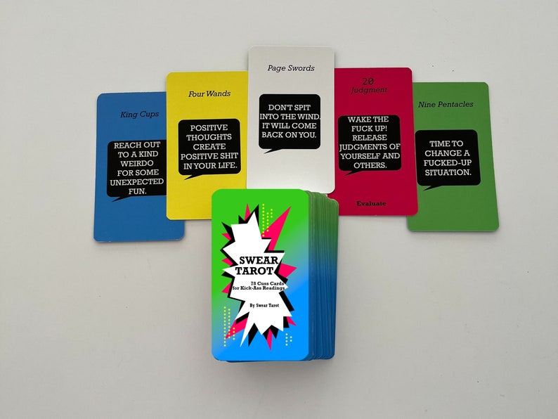 May include: A deck of 78 cards with colourful backs featuring a starburst design. The cards are labelled with the names of tarot cards, such as "King Cups", "Four Wands", "Page Swords", "Judgment", and "Nine Pentacles". The front of the deck features a colourful design with the words "SWEAR TAROT" and "78 Cards for Kick-Ass Readings".