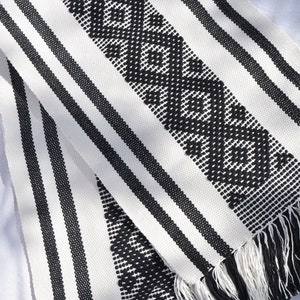 May include: Black and white striped woven table runner with a geometric pattern and fringe on the ends.