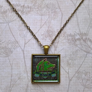 May include: A bronze chain necklace with a square glass pendant featuring a green wolf head with blue text that reads "BOAR".