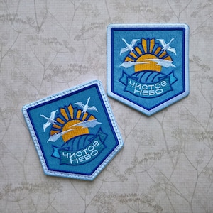 May include: Two blue embroidered patches with a white outline. Each patch features a yellow sun with white clouds, two white birds flying, and a blue banner with the text "Чистое небо" in white.