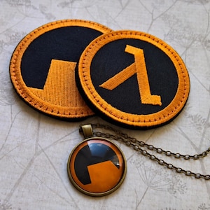 May include: Two circular embroidered patches featuring the orange and black Half-Life lambda symbol and logo, accompanied by a round pendant necklace with a bronze-toned metal frame displaying the orange and black lambda logo.