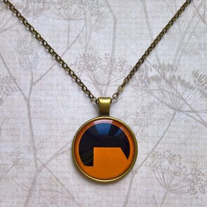 Peut inclure: Un collier en chaîne bronze avec un pendentif rond orné d'un symbole noir et orange. Le symbole est une lettre stylisée "H" avec un sommet incurvé.
