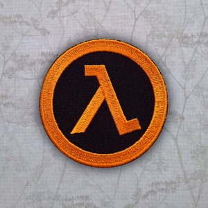 May include: Orange and black embroidered patch featuring the Lambda symbol from the Half-Life video game series.