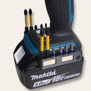 May include: A blue and black Makita 18V lithium-ion battery with a 5.0Ah capacity. The battery has a built-in magnetic bit holder with several different sized bits.