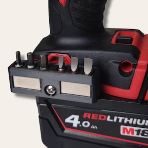 May include: A black and red cordless drill with a magnetic bit holder attached to the side. The bit holder has six slots for different sized bits. The drill battery is labelled "4.0 Ah REDLITHIUM M18".