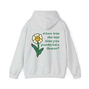 May include: A pale grey hoodie featuring a flower graphic and the text "when was the last time you pondered a flower?" The graphic is a yellow flower with a smiling face and green stem and leaves.