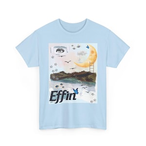May include: Light blue t-shirt featuring a surreal graphic with a crescent moon, ladder, and eye. The design includes butterflies, birds, and the word "Effin" in black and blue. The shirt is a casual wear item.