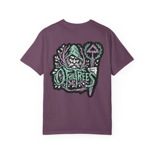 May include: A purple t-shirt featuring a detailed graphic on the back. The design includes a bearded figure in a hooded cloak, surrounded by stylized leaves and the text "OF THE REES" in a whimsical font. The graphic uses shades of green, pink, and white.
