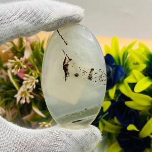 May include: A white agate cabochon with black dendritic inclusions. The agate is oval shaped and has a smooth, polished surface.