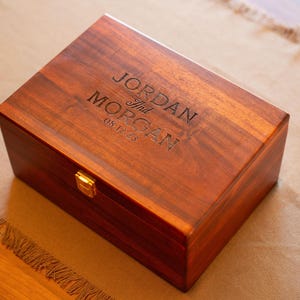 May include: A wooden box with a hinged lid and a brass latch. The box is engraved with the text "Jordan and Morgan 08.12.23".