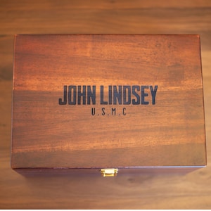 May include: A dark brown wooden box with a brass latch. The box is engraved with the text "JOHN LINDSEY U.S.M.C."
