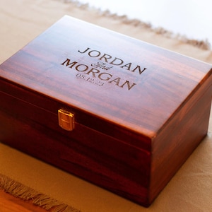 May include: A dark wood box with a brass latch. The box is engraved with the text "JORDAN and MORGAN 08.12.23".