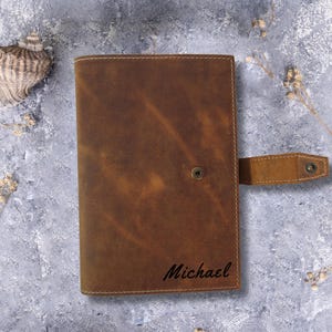 May include: Brown leather journal with a flap closure and a personalized inscription that reads "Michael".