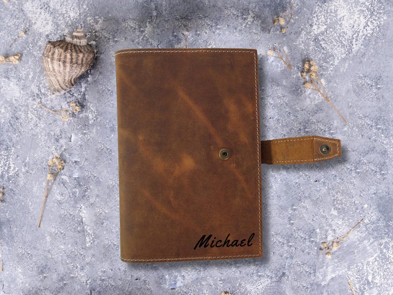 May include: Brown leather journal with a flap closure and a personalized inscription that reads "Michael".