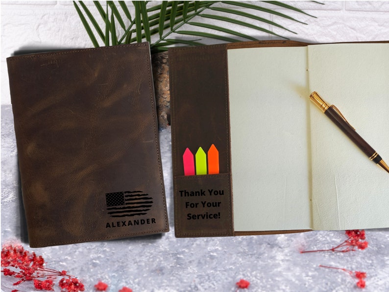 May include: A brown leather journal with a personalized inscription that reads "Thank You For Your Service!" and "ALEXANDER". The journal has a pocket on the front cover with three colorful sticky notes. The journal is open to reveal blank pages and a pen.
