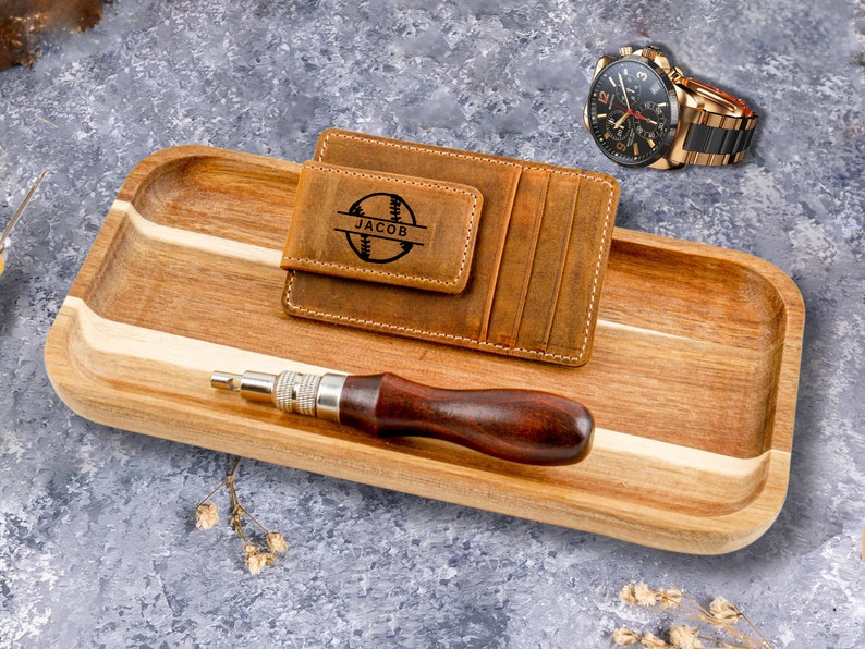 May include: A brown leather wallet with a baseball design and the name "Jacob" engraved on it. The wallet is sitting on a wooden tray with a small screwdriver.
