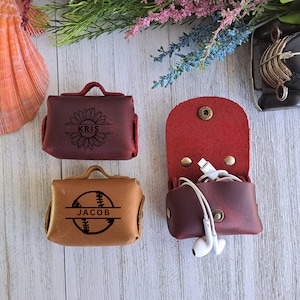 May include: Two personalized leather pouches. One is brown with a baseball graphic and the name "JACOB" engraved on it. The other is burgundy with a sunflower graphic and the name "KRIS" engraved on it.