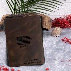 May include: A brown leather journal with a distressed look. The cover features an engraved American flag, the name "JASON", and the text "Thank You For Your Service!"