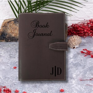 May include: A brown leather journal with the words "Book Journal" embossed on the front cover. The initials "J.D." are also embossed on the front cover.