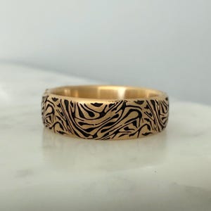May include: A gold band with a black marbled pattern. The band is smooth and polished.